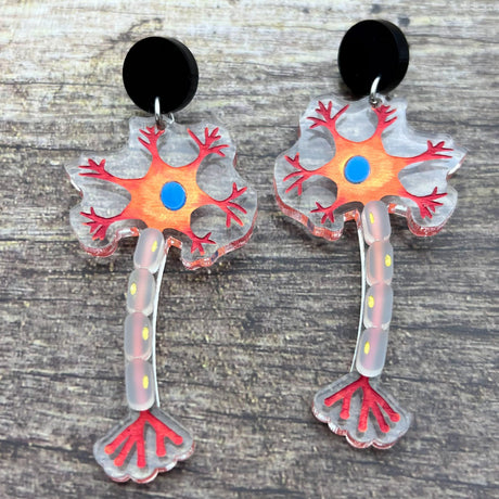 Close up view of laser cut acrylic neuron earrings being modelled. Earrings are cut from transparent acrylic, with the neuron design engraved and handpainted. The neurons hang from black earring toppers. 