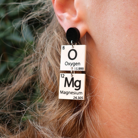 Black and white OMg periodic table earrings being modelled. 