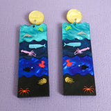 A pair of acrylic earrings featuring the Sunlight, Twilight, Midnight and Abyssal zones, with creatures laser engraved and hand painted within. 