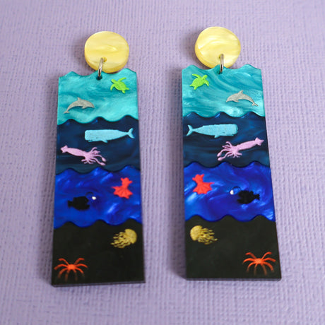 A pair of acrylic earrings featuring the Sunlight, Twilight, Midnight and Abyssal zones, with creatures laser engraved and hand painted within. 
