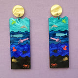 A pair of acrylic earrings featuring the Sunlight, Twilight, Midnight and Abyssal zones, with creatures laser engraved and hand painted within. Front view. 