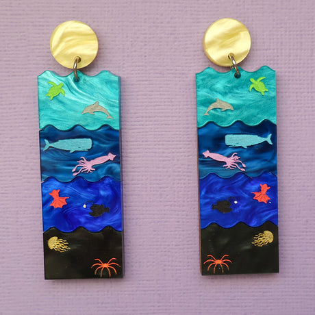 A pair of acrylic earrings featuring the Sunlight, Twilight, Midnight and Abyssal zones, with creatures laser engraved and hand painted within. Front view. 