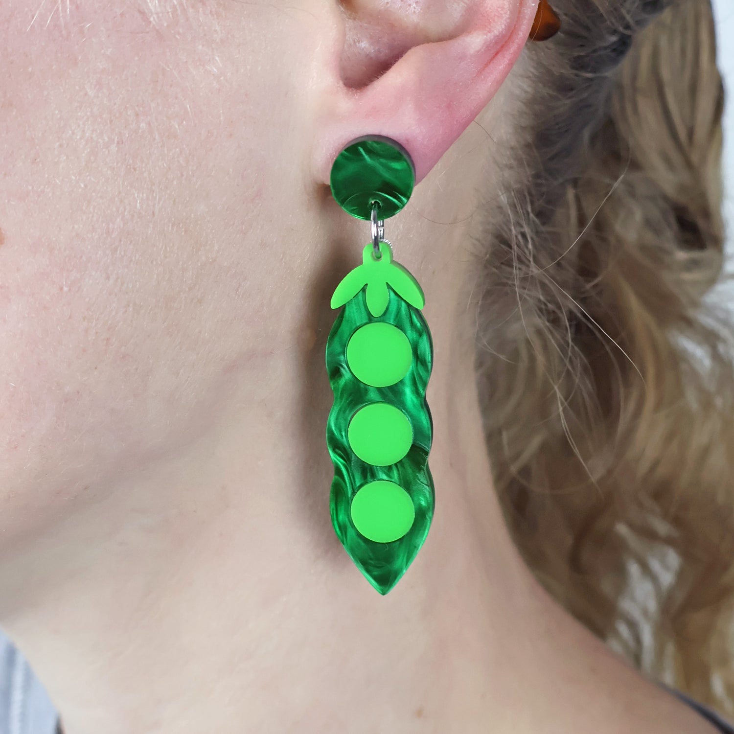 Green acrylic pea pod earrings worn by a person with blonde hair.