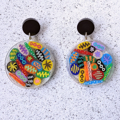 Round earrings resembling Petri Dishes with colourful acrylic shapes arranged within and black acrylic toppers. 