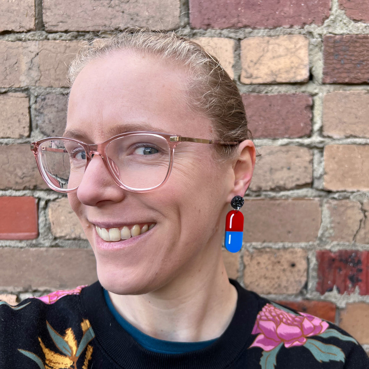 A woman modelling a pair of medicine pill earrings in blue and red