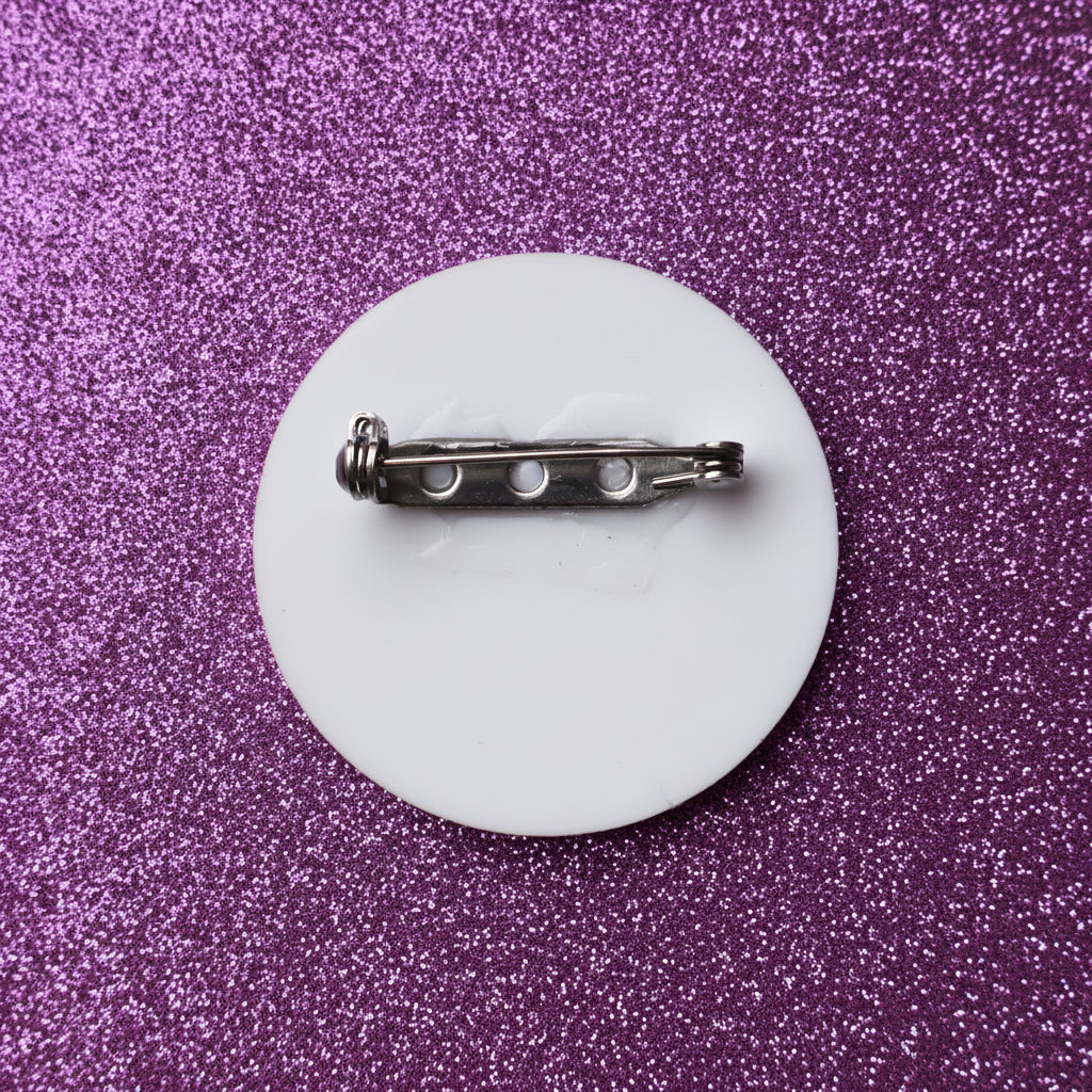 The back of a white round acrylic brooch, showing the stainless steel brooch pin. 