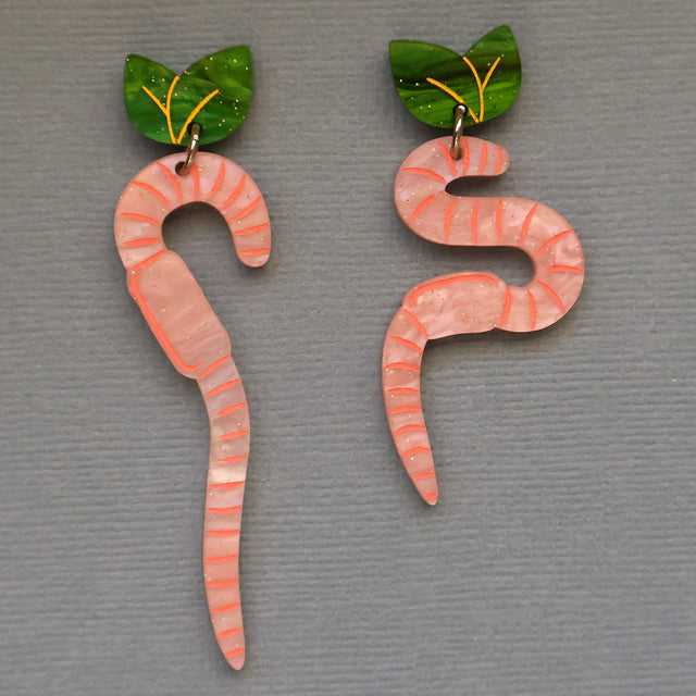 Pair of worm-shaped earrings with green leaf toppers on a grey background