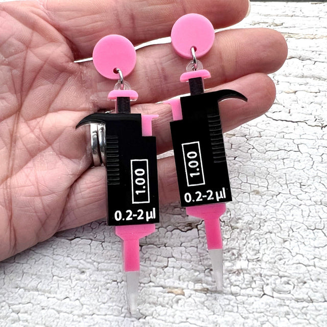Black and Pink laser cut acrylic micropipette earrings, hanging from pink earring toppers.