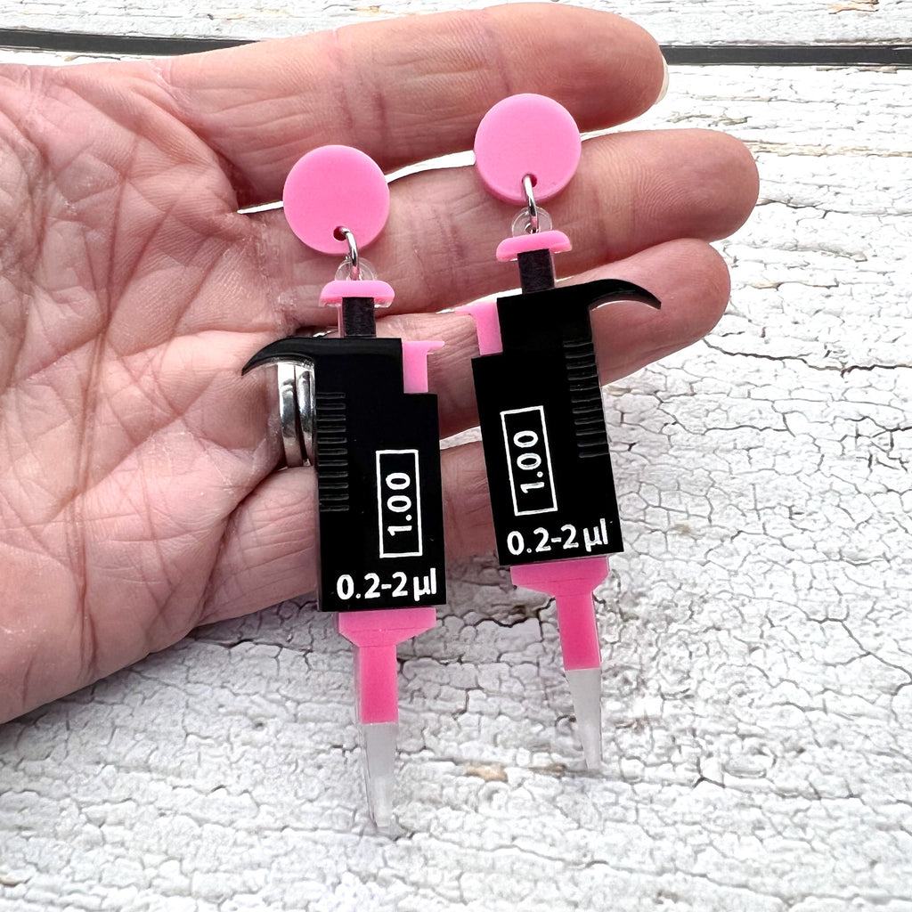 Black and Pink laser cut acrylic micropipette earrings, hanging from pink earring toppers.