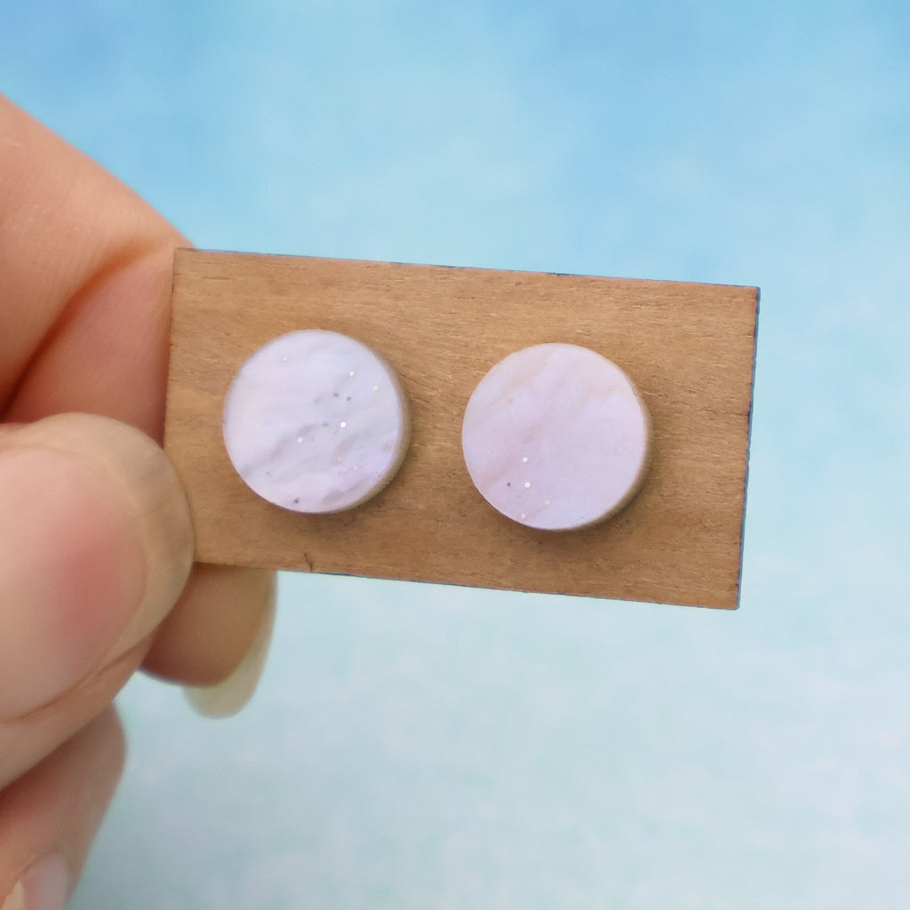 A pair of small pink acrylic studs on a wooden backing card. 