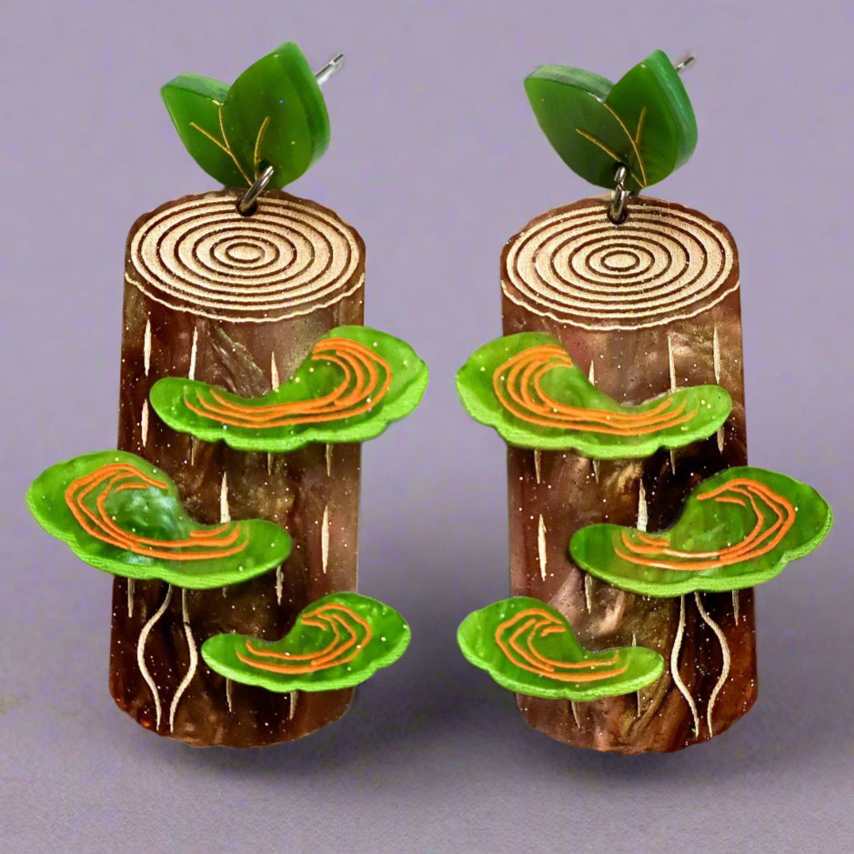 Pair of earrings resembling tree stumps with green shelf fungus growing off them and leafy green acrylic toppers. 