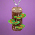 Wooden pendant with  tree trunk, tree rings and green mushrooms being held up. Depicts polypore fungus. 