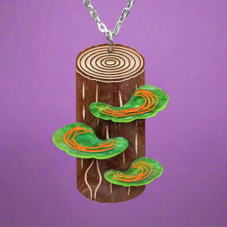 Wooden pendant with  tree trunk, tree rings and green mushrooms being held up. Depicts polypore fungus. 