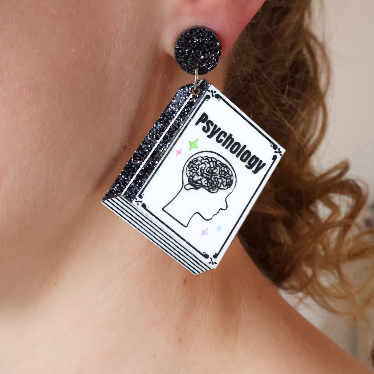Earring with psychology book design and glittery black top worn by a person.