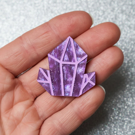 A purple crystal-shaped brooch held in a hand