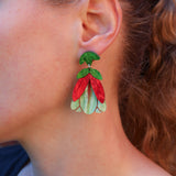 A close-up of a person's ear wearing a colorful flower-shaped dangle earring with green leaves and red and light green petals.