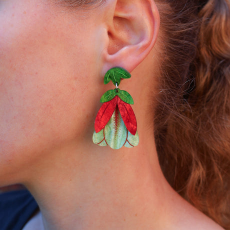 A close-up of a person's ear wearing a colorful flower-shaped dangle earring with green leaves and red and light green petals.