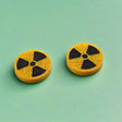 Pair of round yellow glitter stud earrings with black radiation symbol.