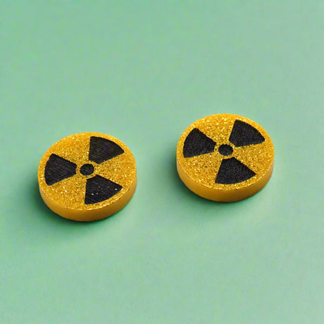 Pair of round yellow glitter stud earrings with black radiation symbol.