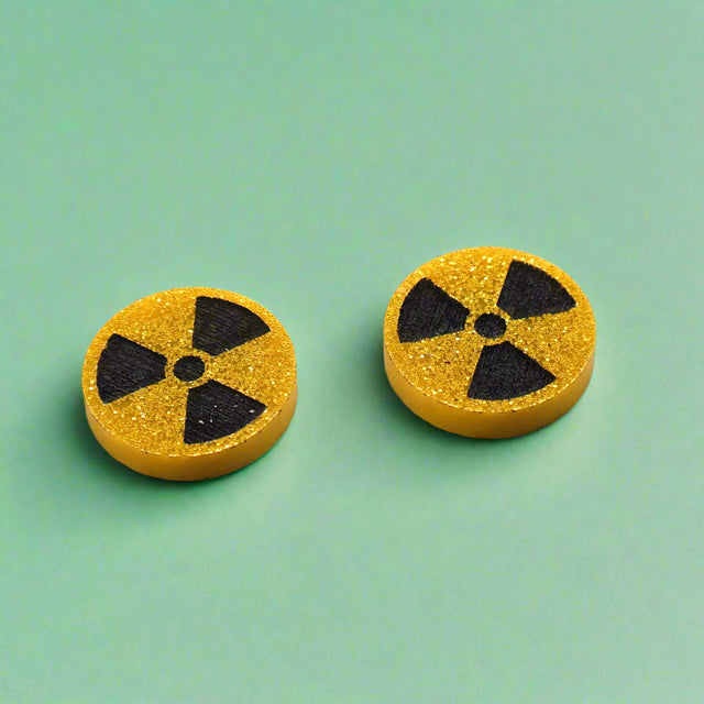 Pair of round yellow glitter stud earrings with black radiation symbol.