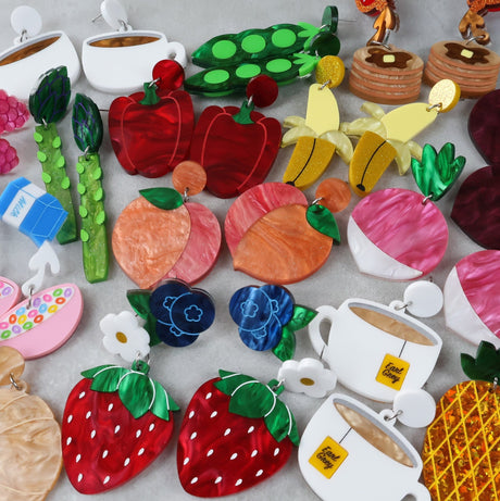 Colorful earrings shaped like fruits, vegetables, and tea cups on a light gray background
