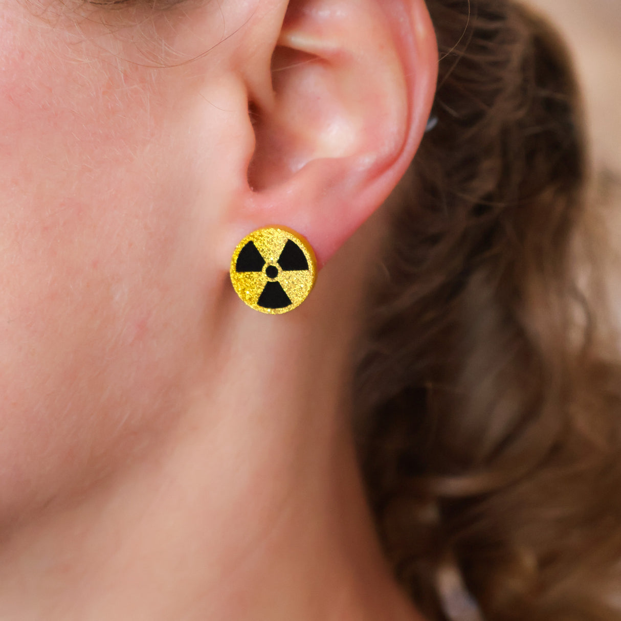 Close-up of an ear wearing a yellow and black radiation symbol earring.