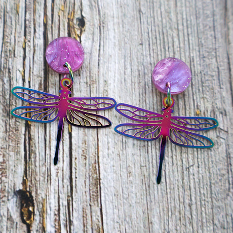 Dragonfly-shaped earrings with purple and blue colours on a wooden surface