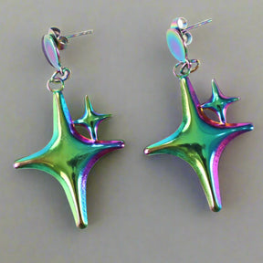 Colorful star-shaped dangle earrings on a light background. This pair is green and purple tinted. 