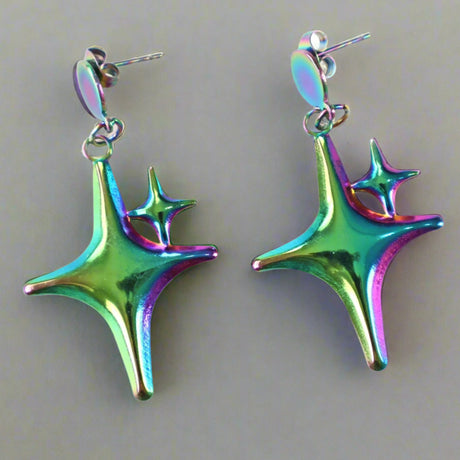 Colorful star-shaped dangle earrings on a light background. This pair is green and purple tinted. 