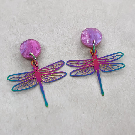 Dragonfly-shaped earrings with purple and blue colours on a light gray background