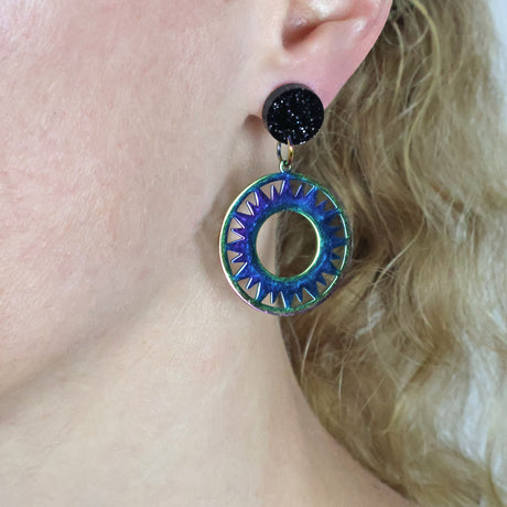 Rainbow tinted stainless steel eclipse dangle earrings with black glittery round acrylic toppers. being modelled. 