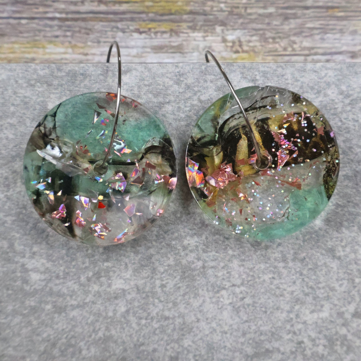 A pair of one of a kind disc shaped recycled acrylic earrings on stainless steel hoops with green and pink acrylics titled 'Enchanted Forest'. Pair 03-11