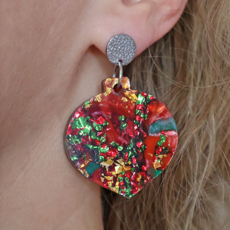 A pair of one of a kind recycled acrylic Christmas bauble earrings with stainless steel toppers, featuring a red, green and gold acrylic design being modelled.