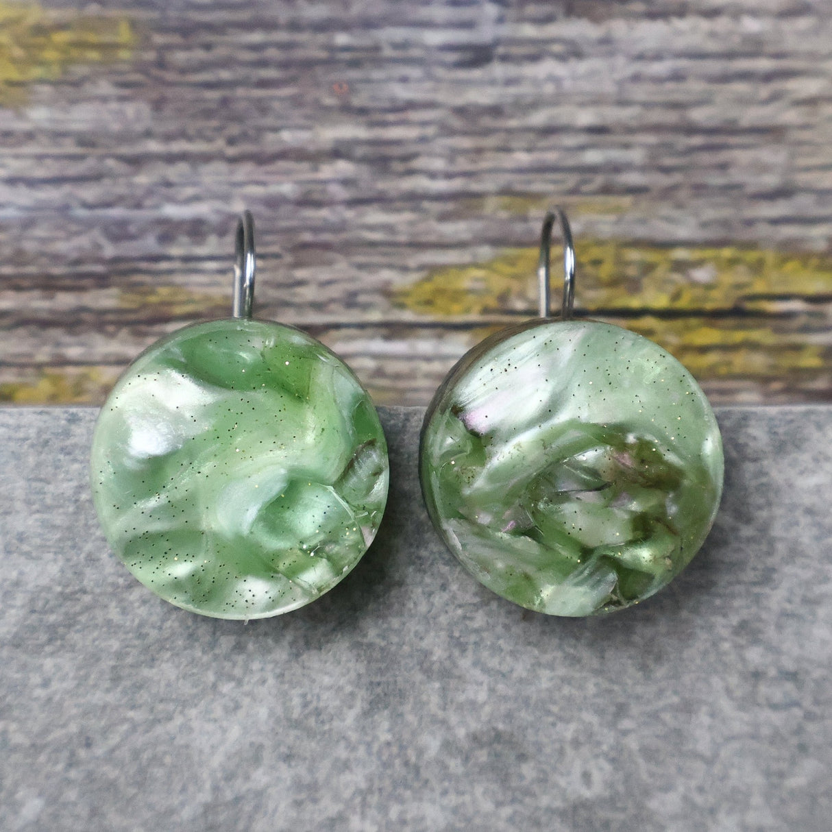 A pair of one of a kind round recycled acrylic earrings with stainless steel french hooks and green acrylics titled  'Green Ripple'. 