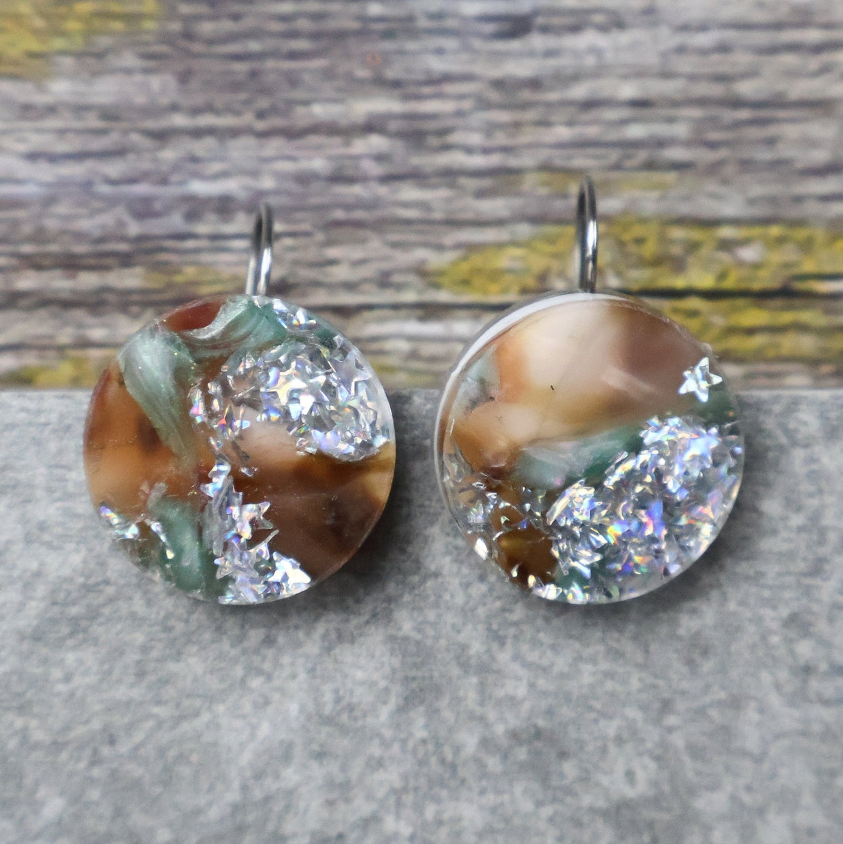 A pair of one of a kind round recycled acrylic earrings with stainless steel french hooks and green silver and brown acrylics titled  'Celestial Tide'. 