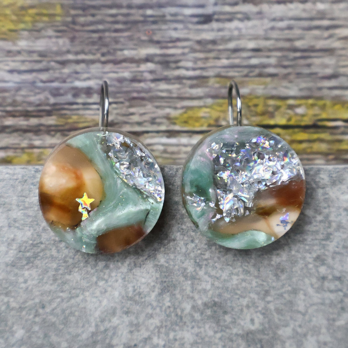 A pair of one of a kind round recycled acrylic earrings with stainless steel french hooks and green silver and brown acrylics titled  'Celestial Tide'. 