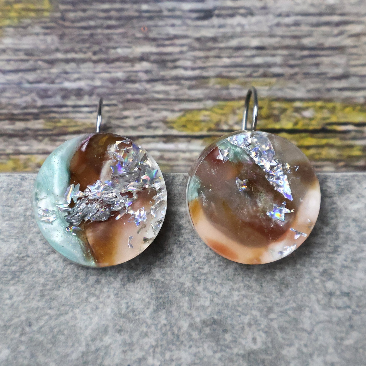 A pair of one of a kind round recycled acrylic earrings with stainless steel french hooks and green silver and brown acrylics titled  'Celestial Tide'. 