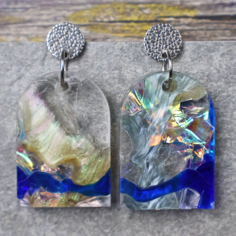 A pair of one of a kind arch shaped recycled acrylic earrings with blue, clear and pearlescent acrylics titled  'Aurora Shards' and stainless steel toppers. Pair 100-01