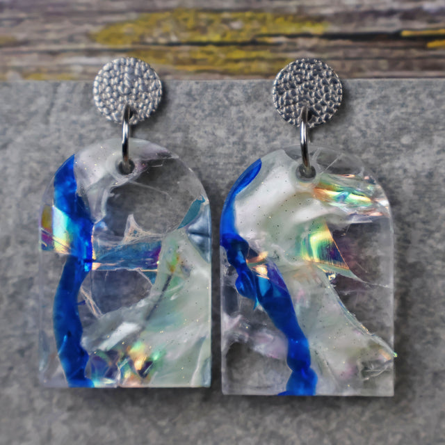 A pair of one of a kind arch shaped recycled acrylic earrings with blue, clear and pearlescent acrylics titled  'Aurora Shards' and stainless steel toppers. Pair 100-02