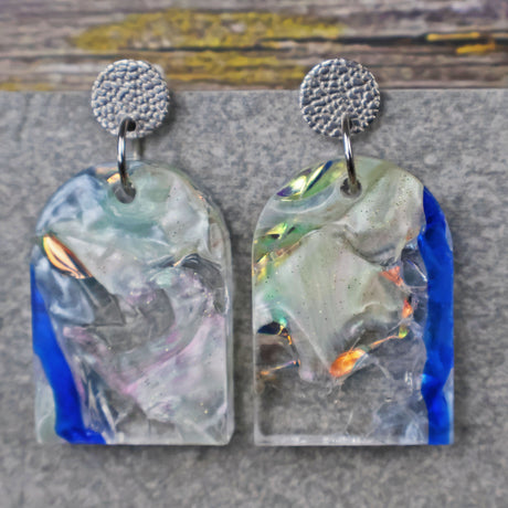 A pair of one of a kind arch shaped recycled acrylic earrings with blue, clear and pearlescent acrylics titled  'Aurora Shards' and stainless steel toppers. Pair 100-03