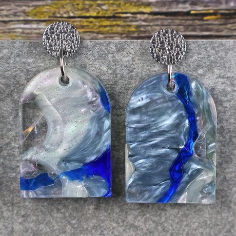 A pair of one of a kind arch shaped recycled acrylic earrings with blue, clear and pearlescent acrylics titled  'Aurora Shards' and stainless steel toppers. Pair 100-06