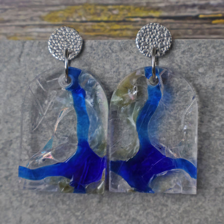 A pair of one of a kind arch shaped recycled acrylic earrings with blue, clear and pearlescent acrylics titled  'Aurora Shards' and stainless steel toppers. Pair 100-07