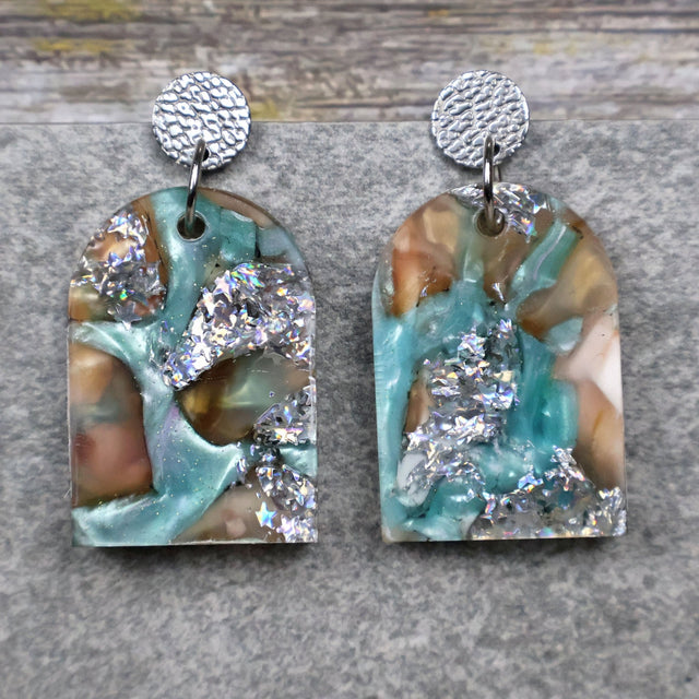 A pair of one of a kind arch shaped recycled acrylic earrings with silver, green and brown design titled 'Celestial Tide' and stainless steel toppers. Pair 102-01