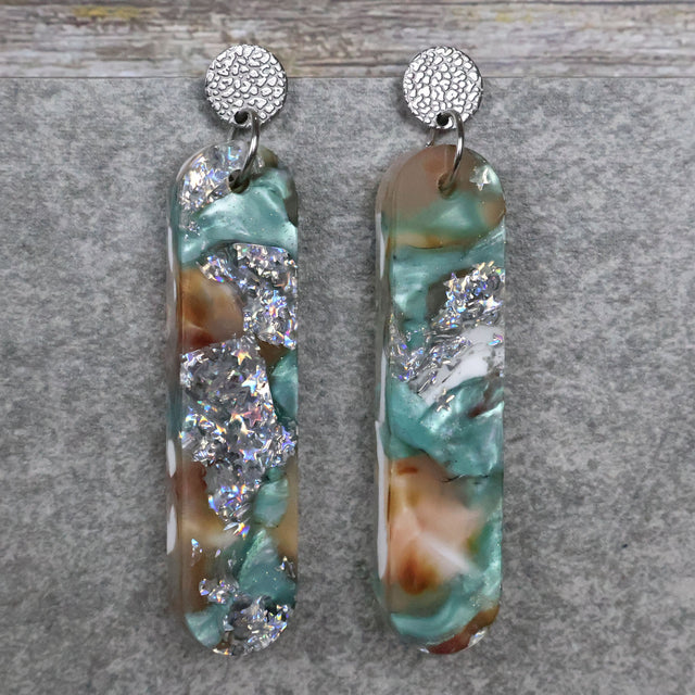 A pair of one of a kind long oval shaped recycled acrylic earrings with silver, green and pink design titled 'Celestial Tide' and stainless steel toppers. Pair 102-12