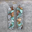 A pair of one of a kind long oval shaped recycled acrylic earrings with silver, green and brown design titled 'Celestial Tide' and stainless steel toppers. Pair 102-13