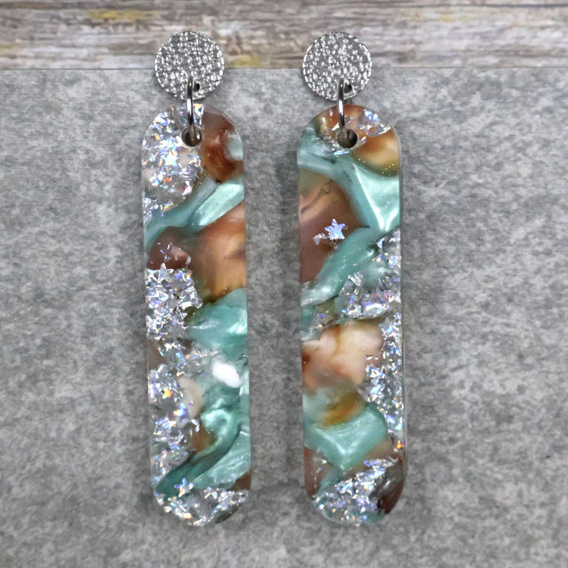 A pair of one of a kind long oval shaped recycled acrylic earrings with silver, green and brown design titled 'Celestial Tide' and stainless steel toppers. Pair 102-13