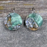A pair of one of a kind round recycled acrylic earrings with stainless steel french hooks and silver, green and brown design titled 'Celestial Tide' Pair 106-14
