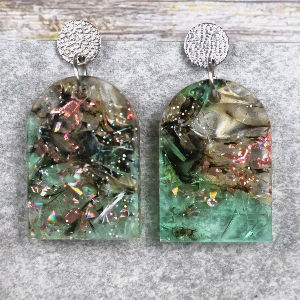 A pair of one of a kind arch shaped recycled acrylic earrings with green and pink design titled 'Enchanted Forest' and stainless steel toppers. Pair 103-03