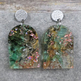 A pair of one of a kind arch shaped recycled acrylic earrings with green and pink design titled 'Enchanted Forest' and stainless steel toppers. Pair 103-04