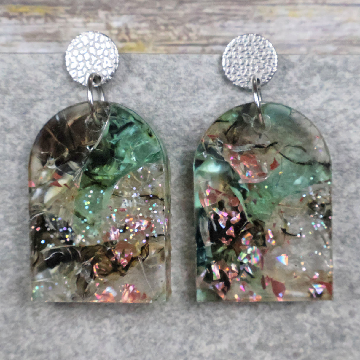 A pair of one of a kind arch shaped recycled acrylic earrings with green and pink design titled 'Enchanted Forest' and stainless steel toppers. Pair 103-07